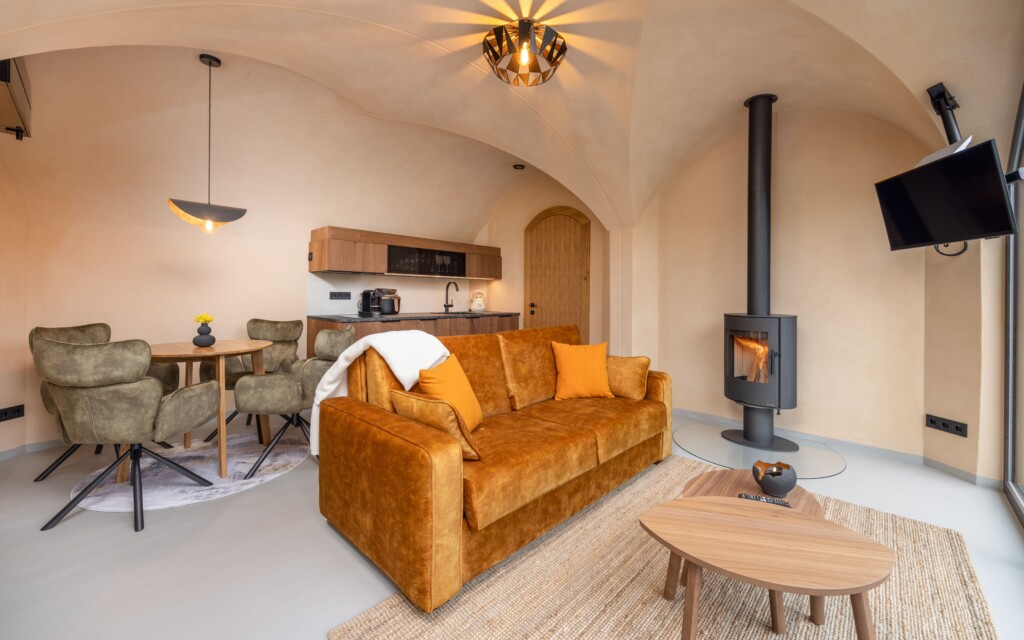 Revonia underground house living room – arched vault interior with orange sofa, wood stove and dining area in modular earth home